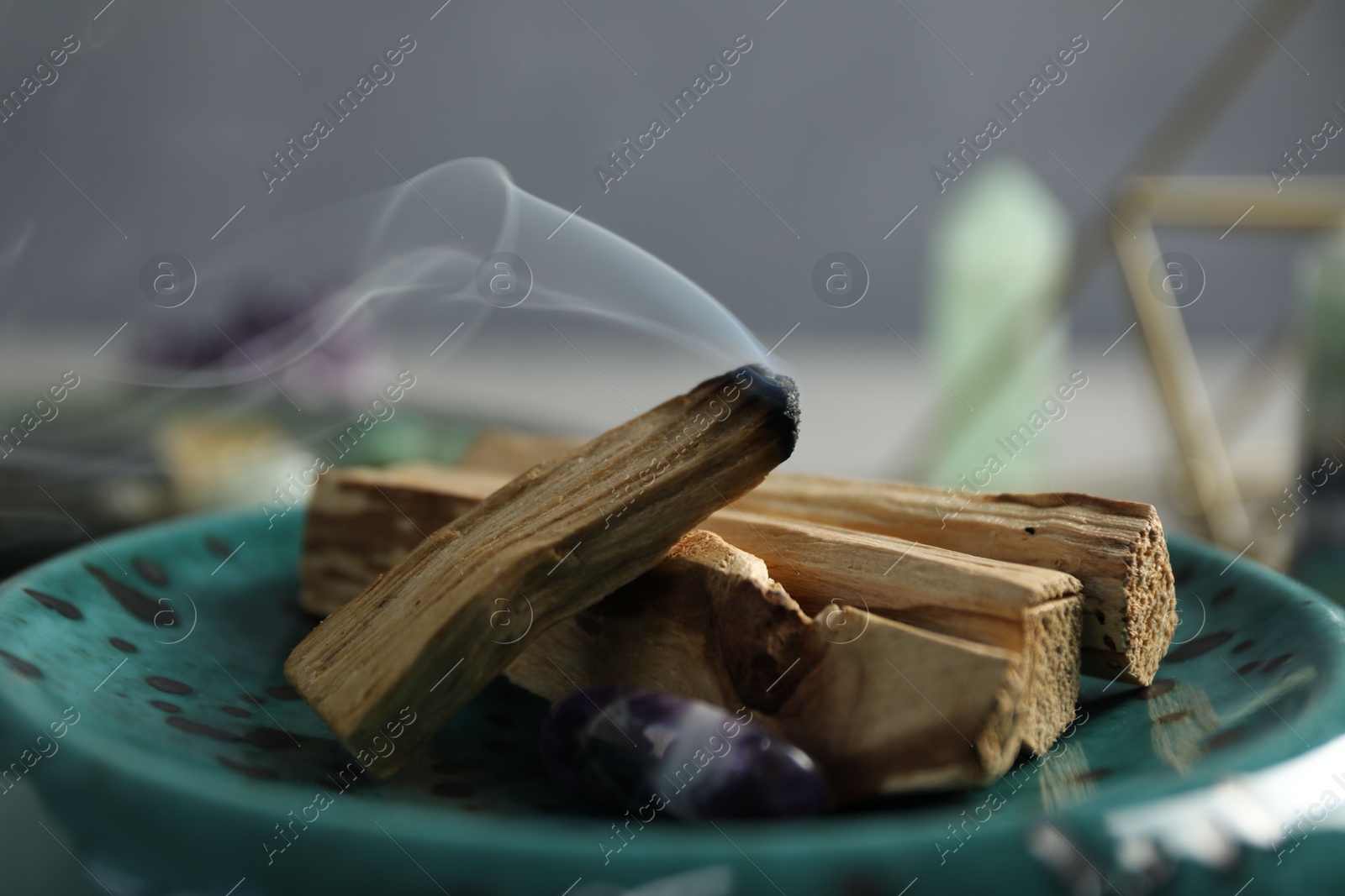 Photo of Smoldering palo santo stick and gemstone on table, closeup