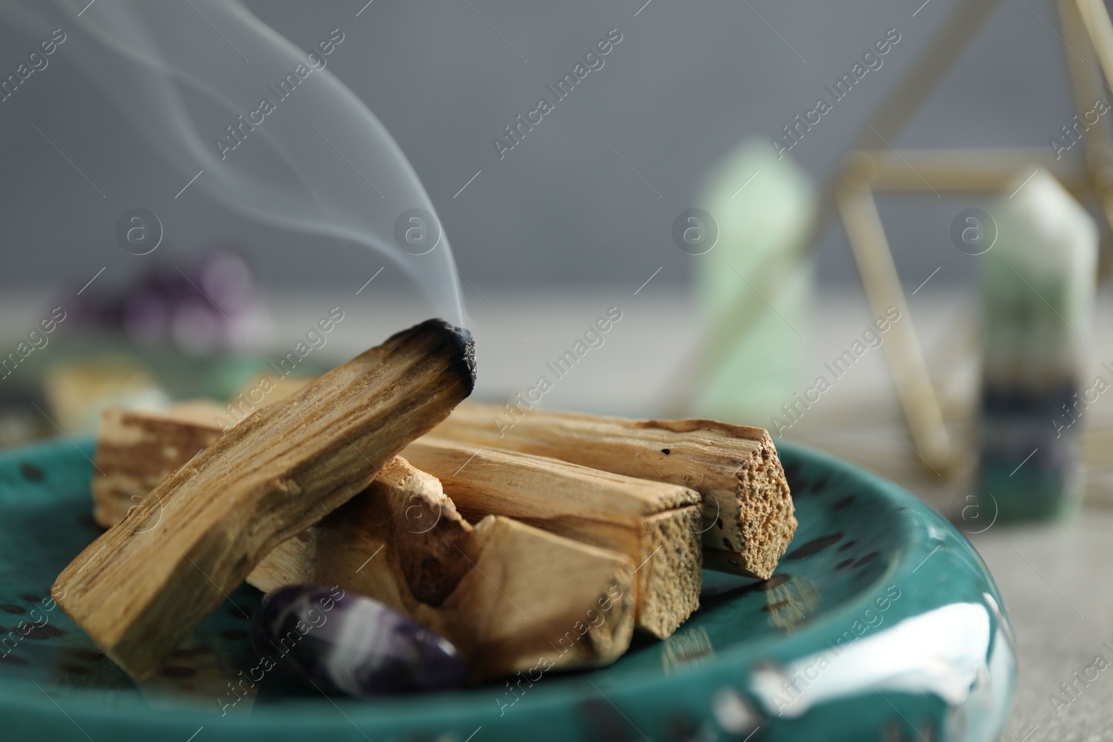 Photo of Smoldering palo santo stick and gemstone on table, closeup