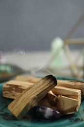 Photo of Smoldering palo santo stick and gemstone on table, closeup