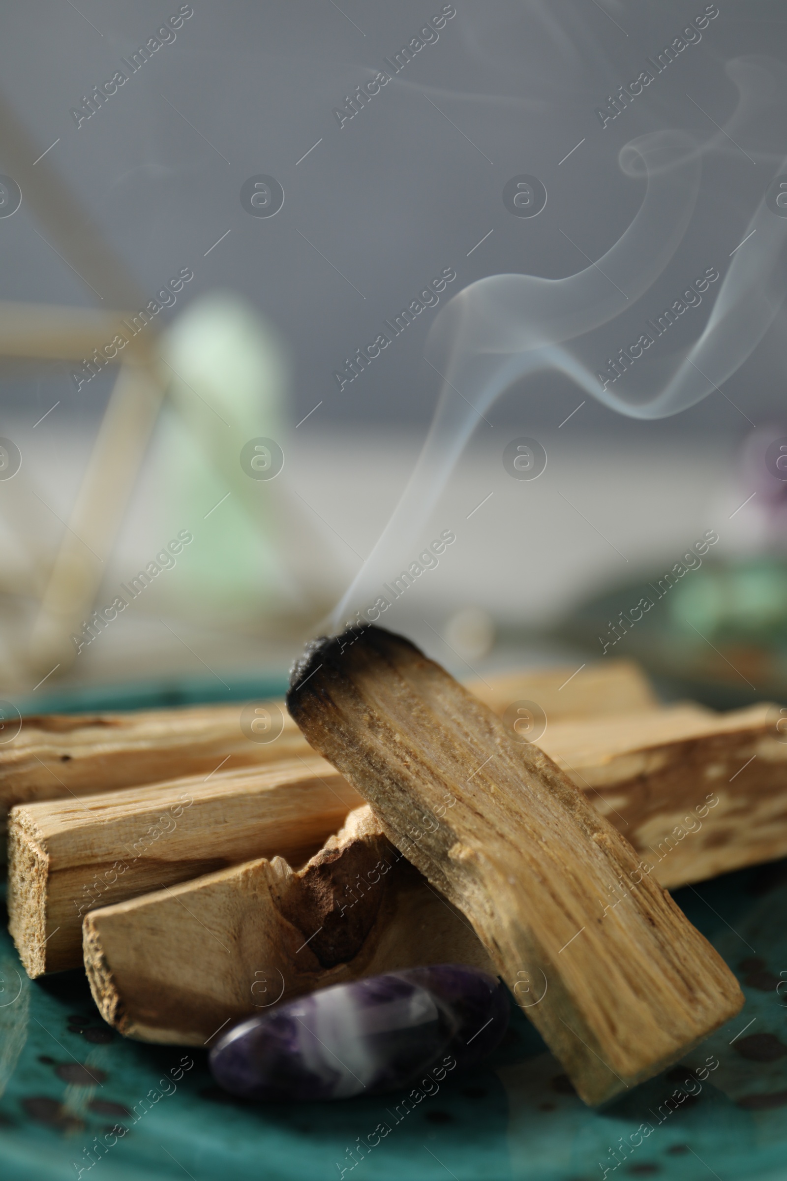 Photo of Smoldering palo santo stick and gemstone on table, closeup