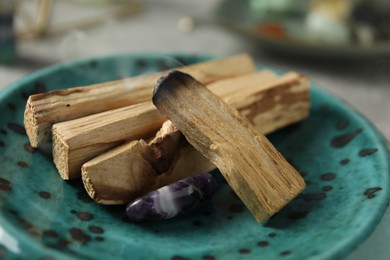 Photo of Smoldering palo santo stick and gemstone on table, closeup