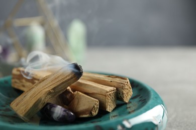 Photo of Smoldering palo santo stick and gemstone on table, closeup