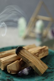 Photo of Smoldering palo santo stick and gemstone on table, closeup