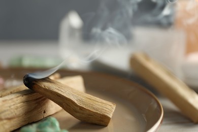 Photo of Burning palo santo stick and gemstone on table, closeup. Space for text