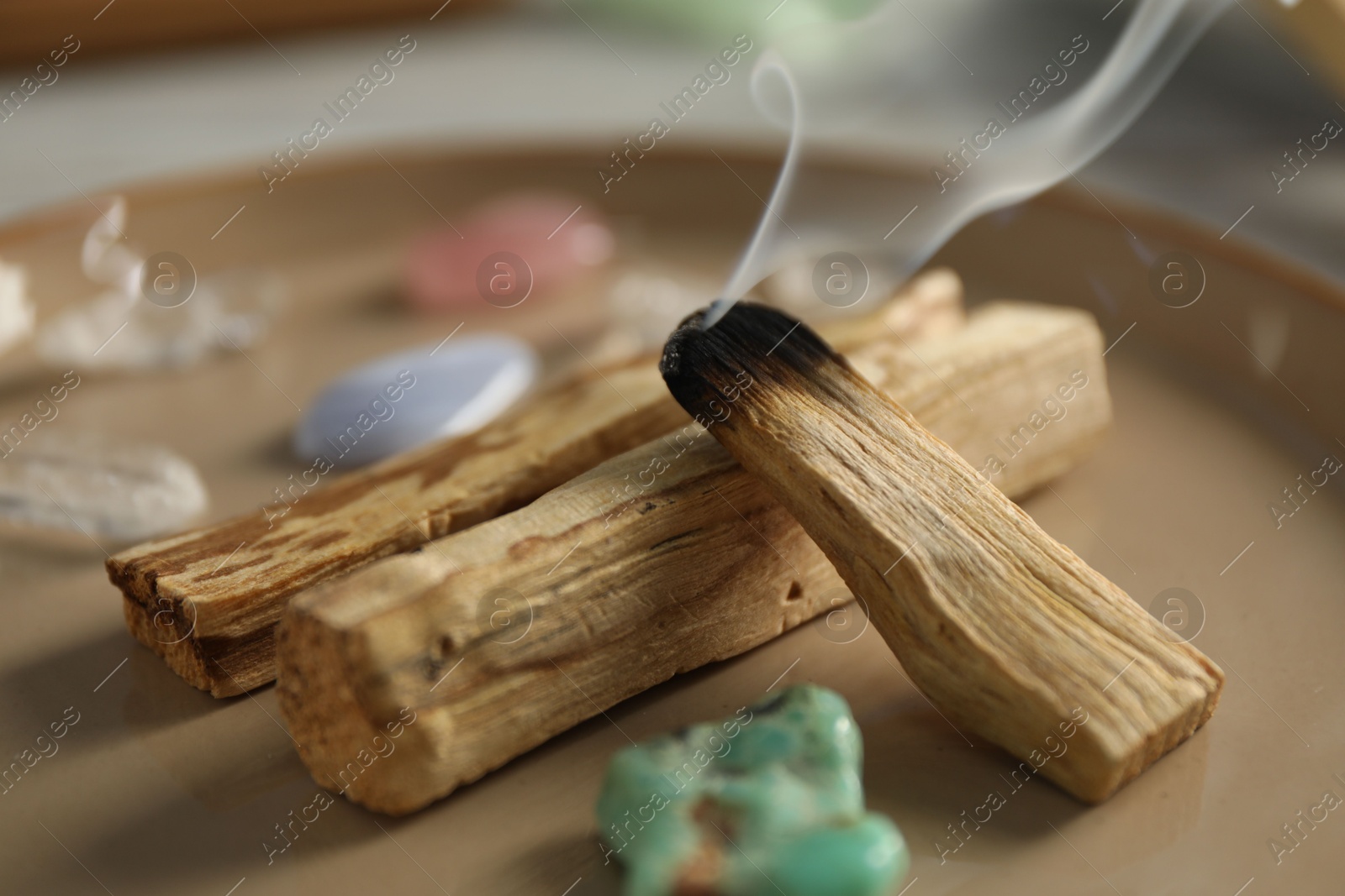 Photo of Smoldering palo santo stick and gemstones on plate, closeup