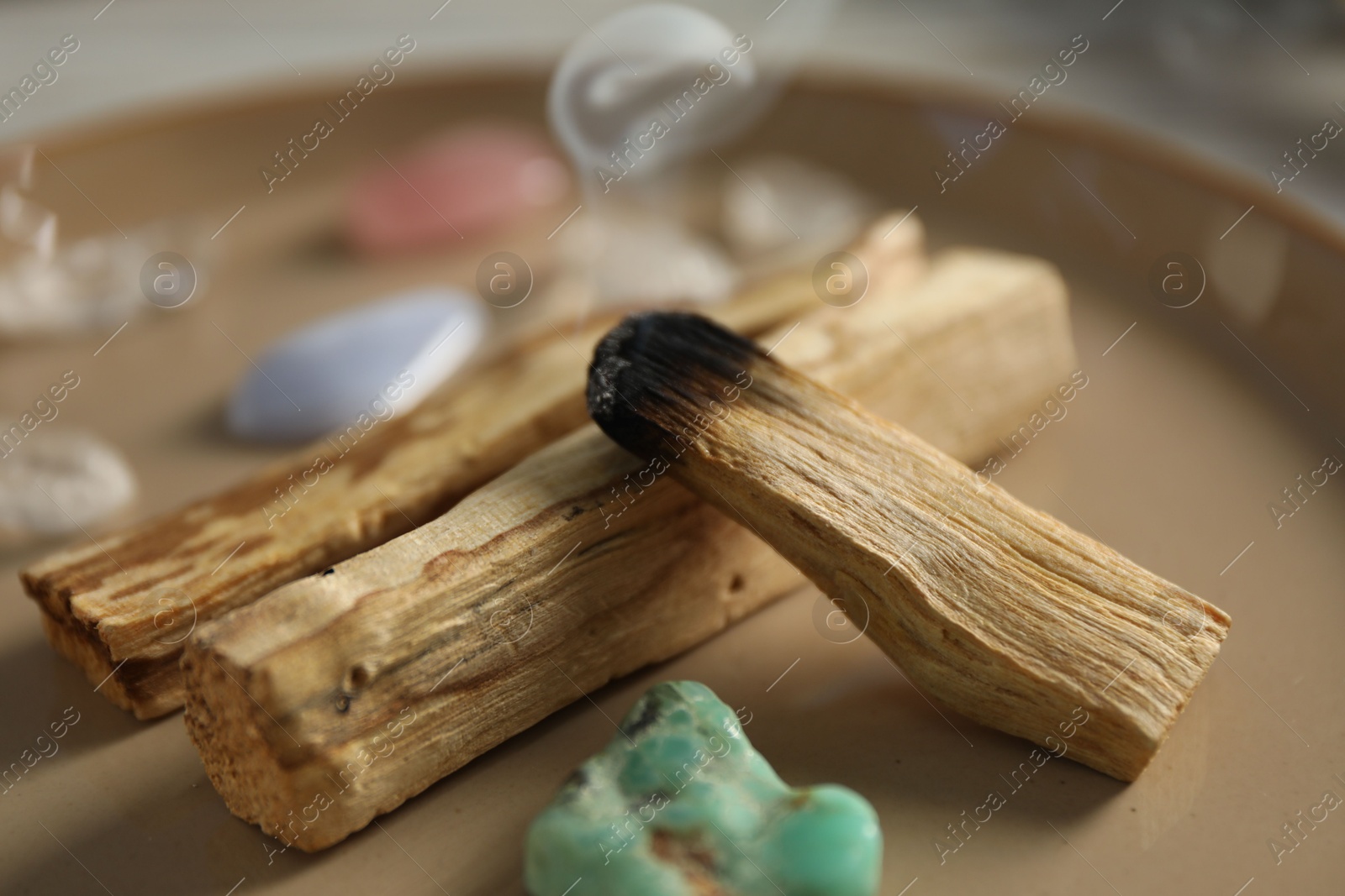 Photo of Smoldering palo santo stick and gemstones on plate, closeup