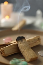 Photo of Smoldering palo santo stick and gemstones on plate, closeup