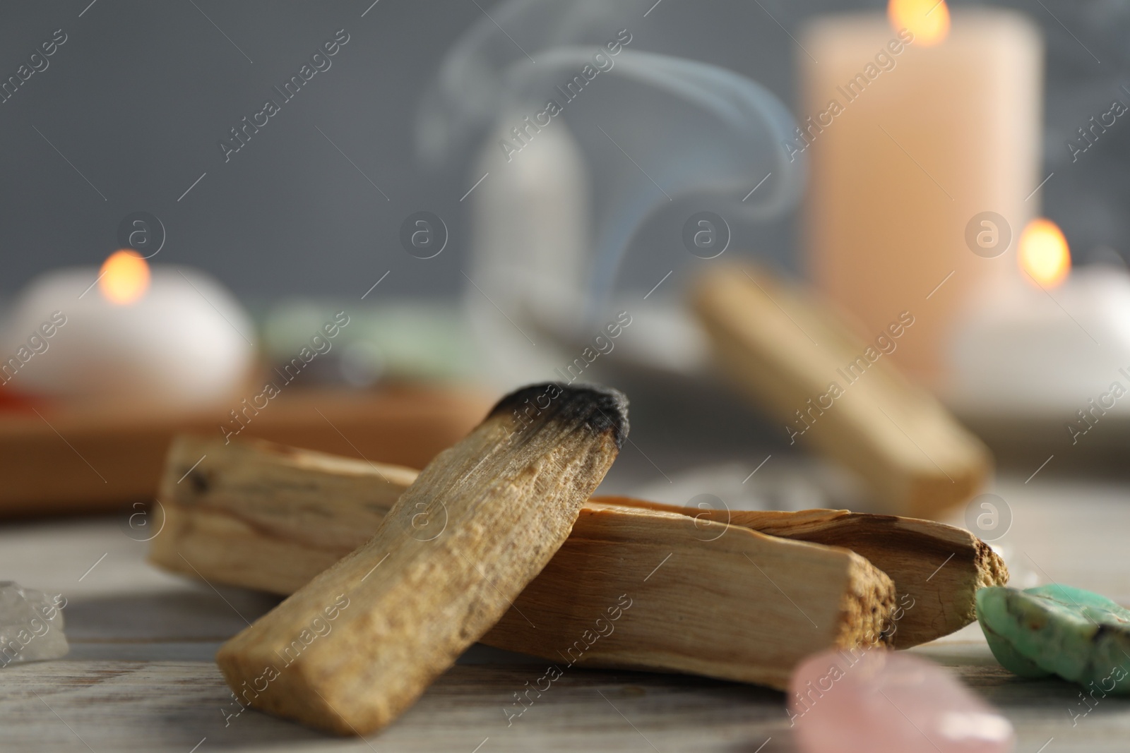 Photo of Smoldering palo santo stick and gemstones on wooden table, closeup