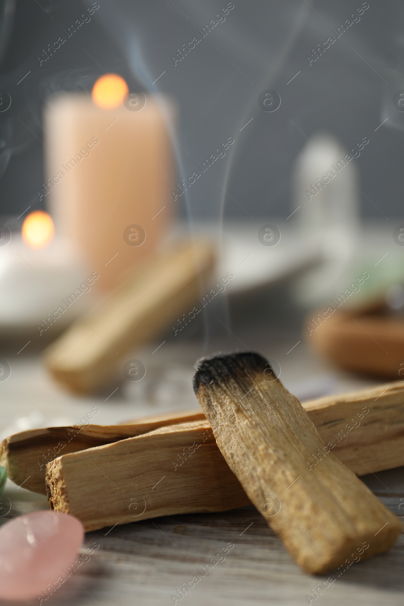 Photo of Smoldering palo santo stick and gemstone on wooden table, closeup