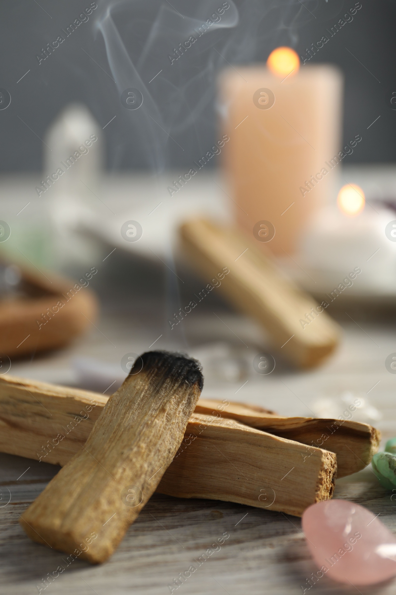 Photo of Smoldering palo santo stick and gemstone on wooden table, closeup