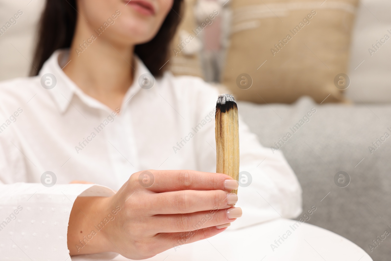 Photo of Woman with burnt palo santo stick at home, selective focus