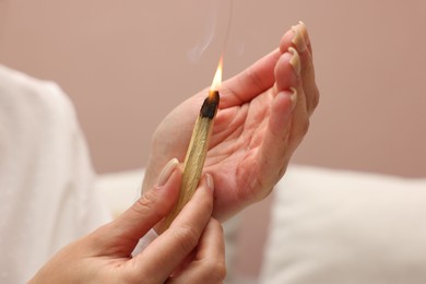 Photo of Woman with burning palo santo stick at home, closeup