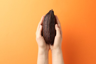 Photo of Woman with cocoa pod on orange background, closeup