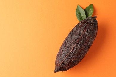 Photo of Natural cocoa pod on orange background, top view. Space for text