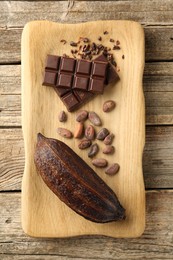 Photo of Cocoa pod, beans and chocolate on wooden table, top view