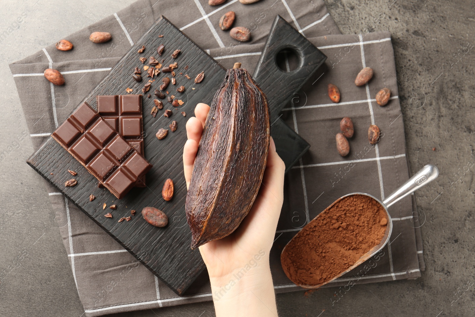 Photo of Woman with cocoa pod, beans, powder and chocolate at grey table, top view