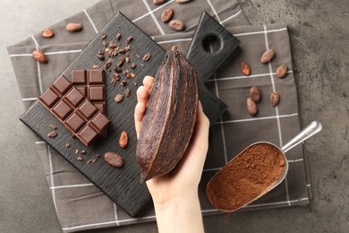 Photo of Woman with cocoa pod, beans, powder and chocolate at grey table, top view