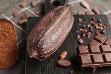 Photo of Cocoa pod, beans, powder and chocolate on grey table, closeup