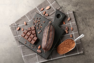 Cocoa pod, beans, powder and chocolate on grey table, flat lay