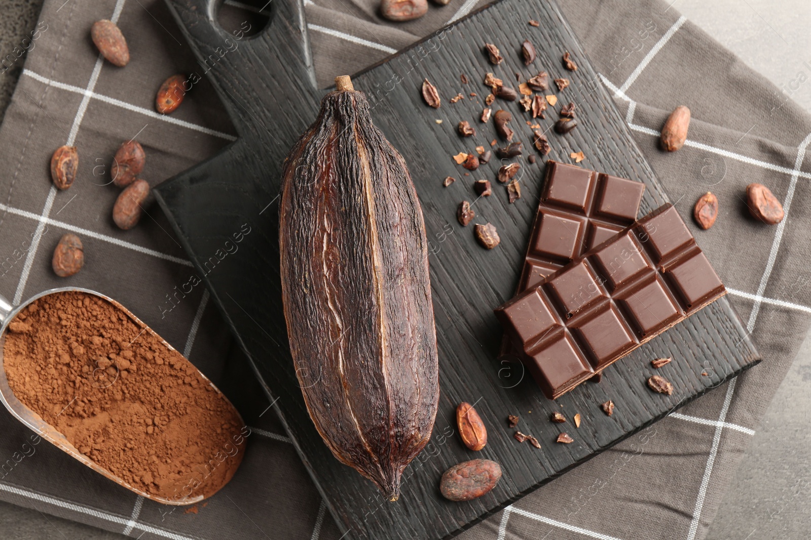 Photo of Cocoa pod, beans, powder and chocolate on grey table, flat lay