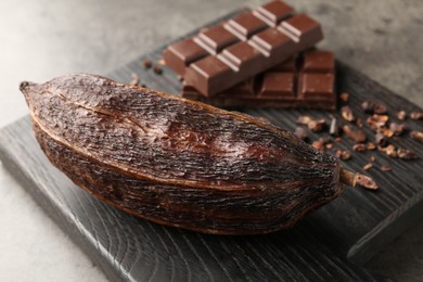 Photo of Cocoa pod and chocolate on grey table, closeup