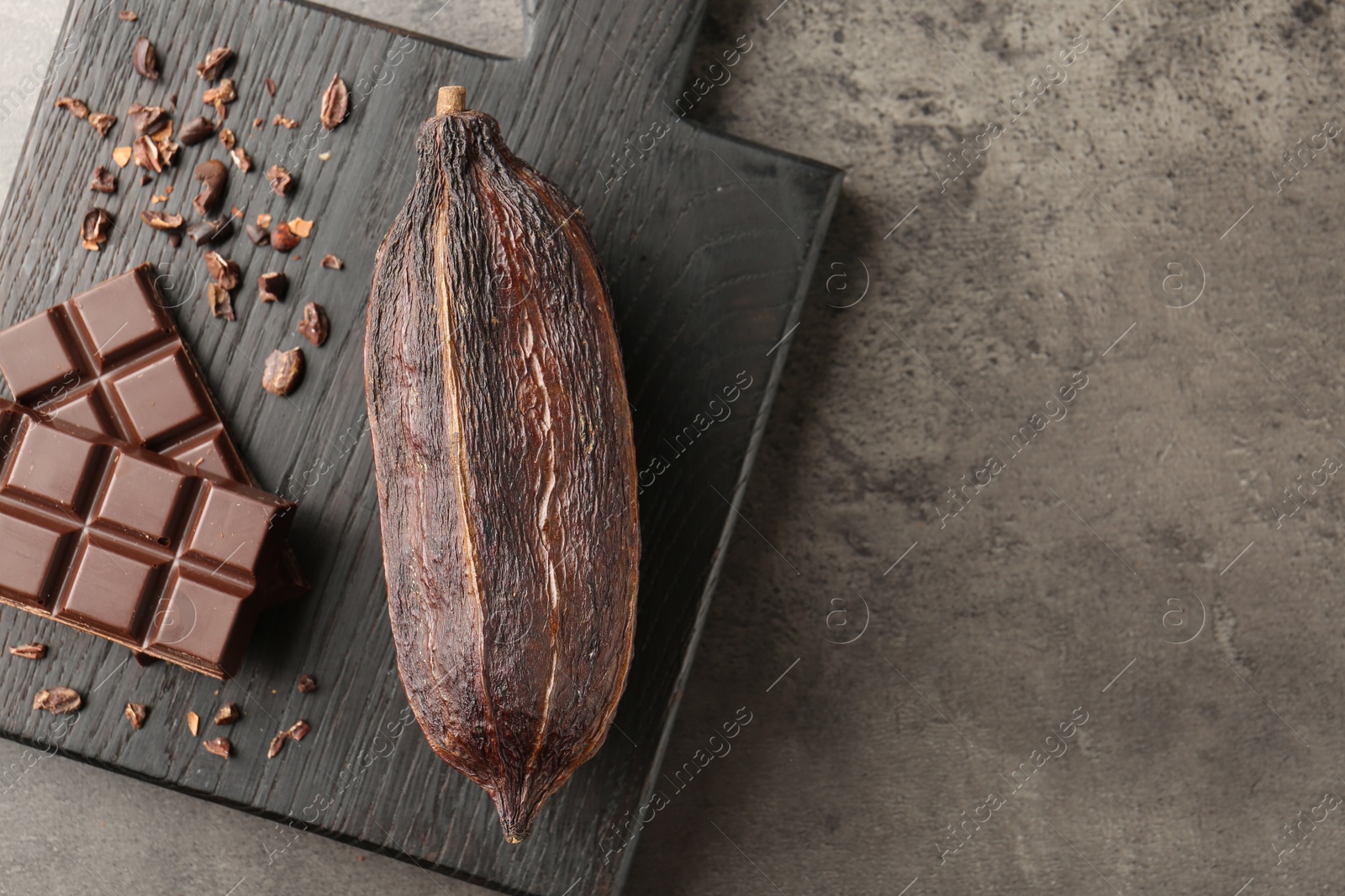 Photo of Cocoa pod and chocolate on grey table, top view. Space for text