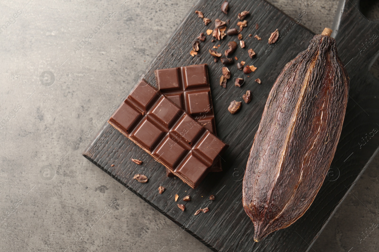 Photo of Cocoa pod and chocolate on grey table, top view. Space for text