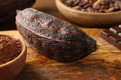 Photo of Cocoa pod, beans, powder and chocolate on wooden table, closeup