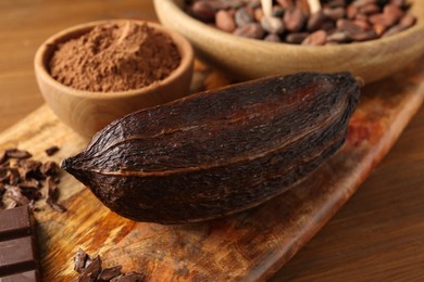 Cocoa pod, beans, powder and chocolate on wooden table, closeup