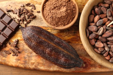 Cocoa pod, beans, powder and chocolate on wooden table, top view