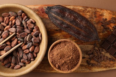 Cocoa pod, beans and powder on brown background, top view