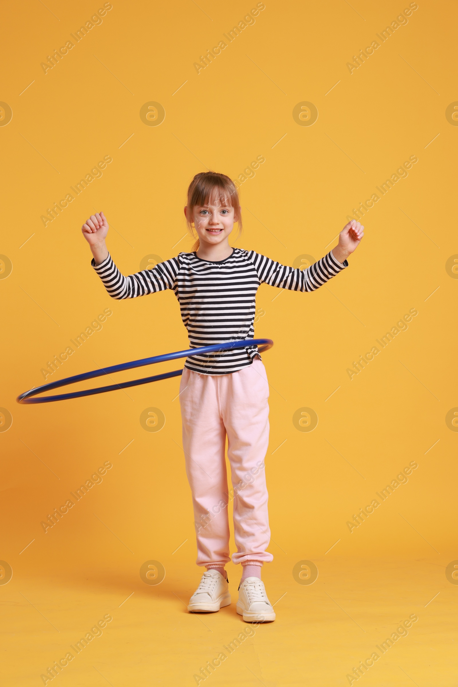 Photo of Cute little girl exercising with hula hoop on orange background