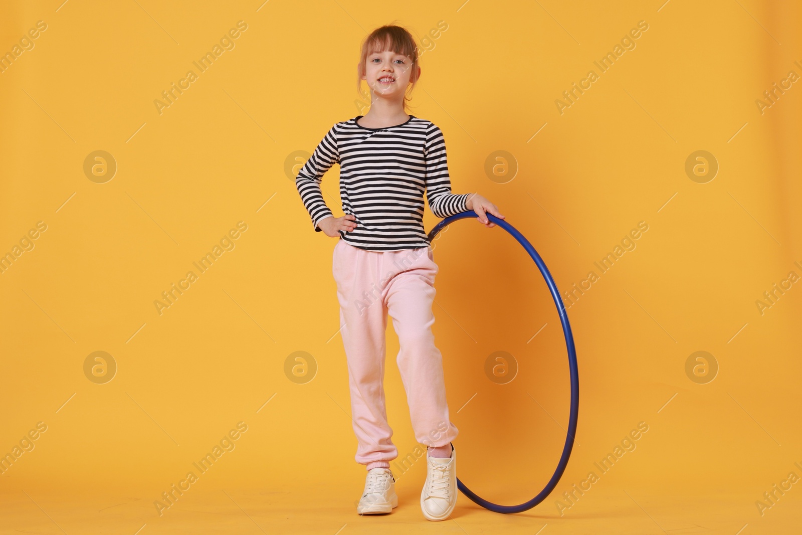 Photo of Cute little girl with hula hoop on orange background