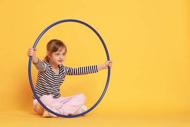 Photo of Cute little girl with hula hoop on orange background, space for text