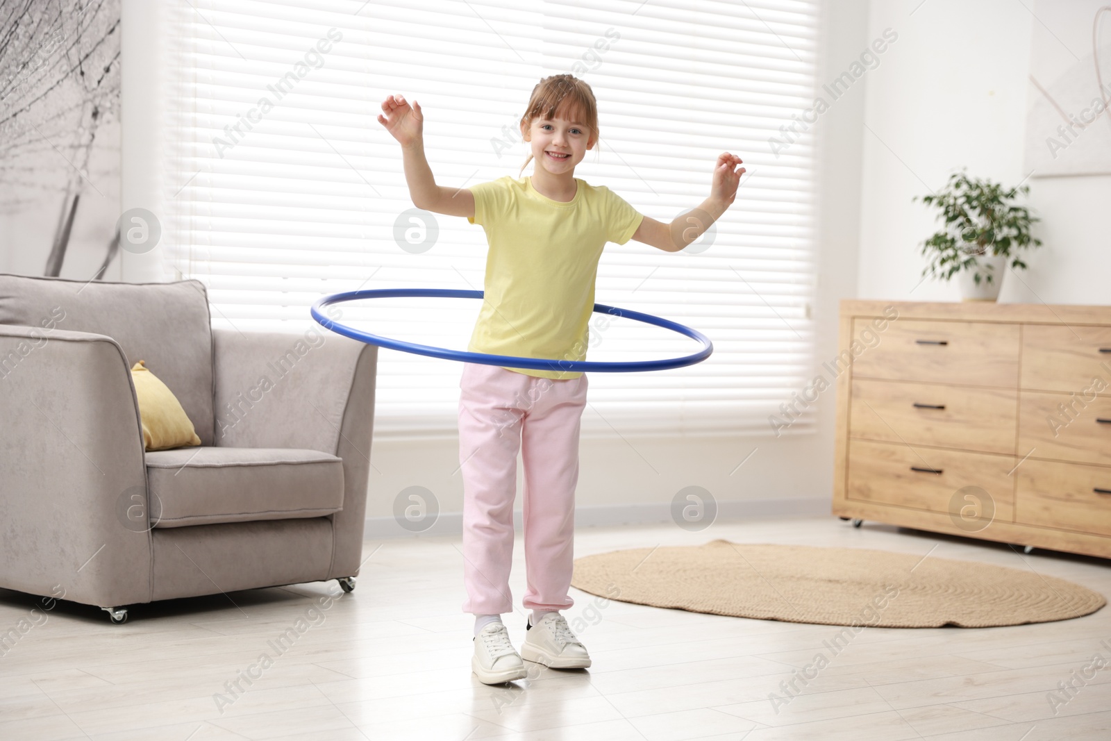 Photo of Cute little girl exercising with hula hoop at home