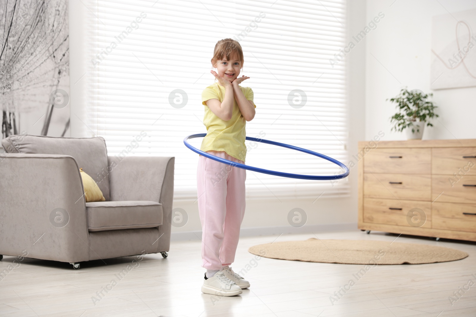 Photo of Cute little girl exercising with hula hoop at home