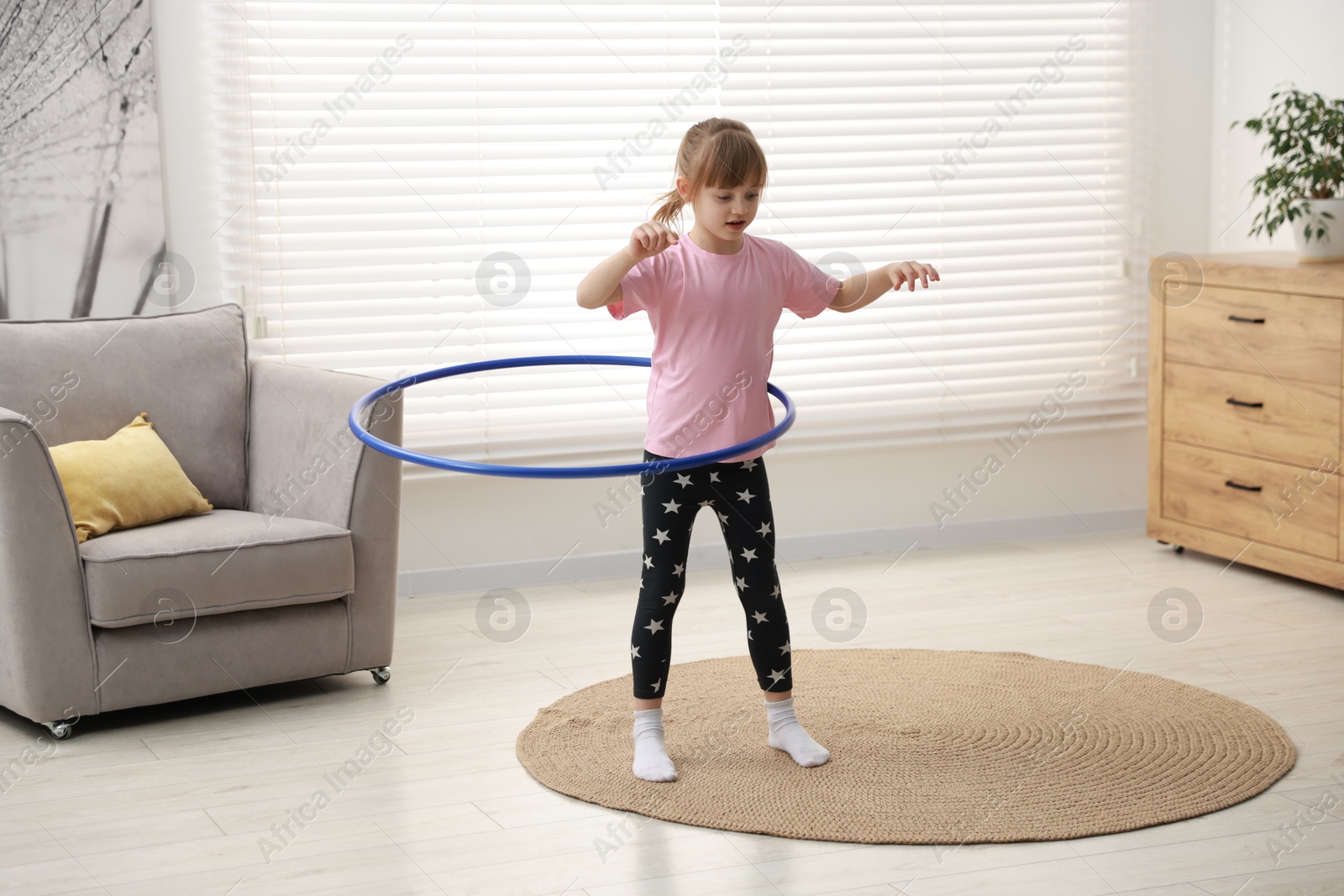 Photo of Cute little girl exercising with hula hoop at home