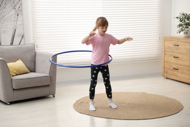 Photo of Cute little girl exercising with hula hoop at home