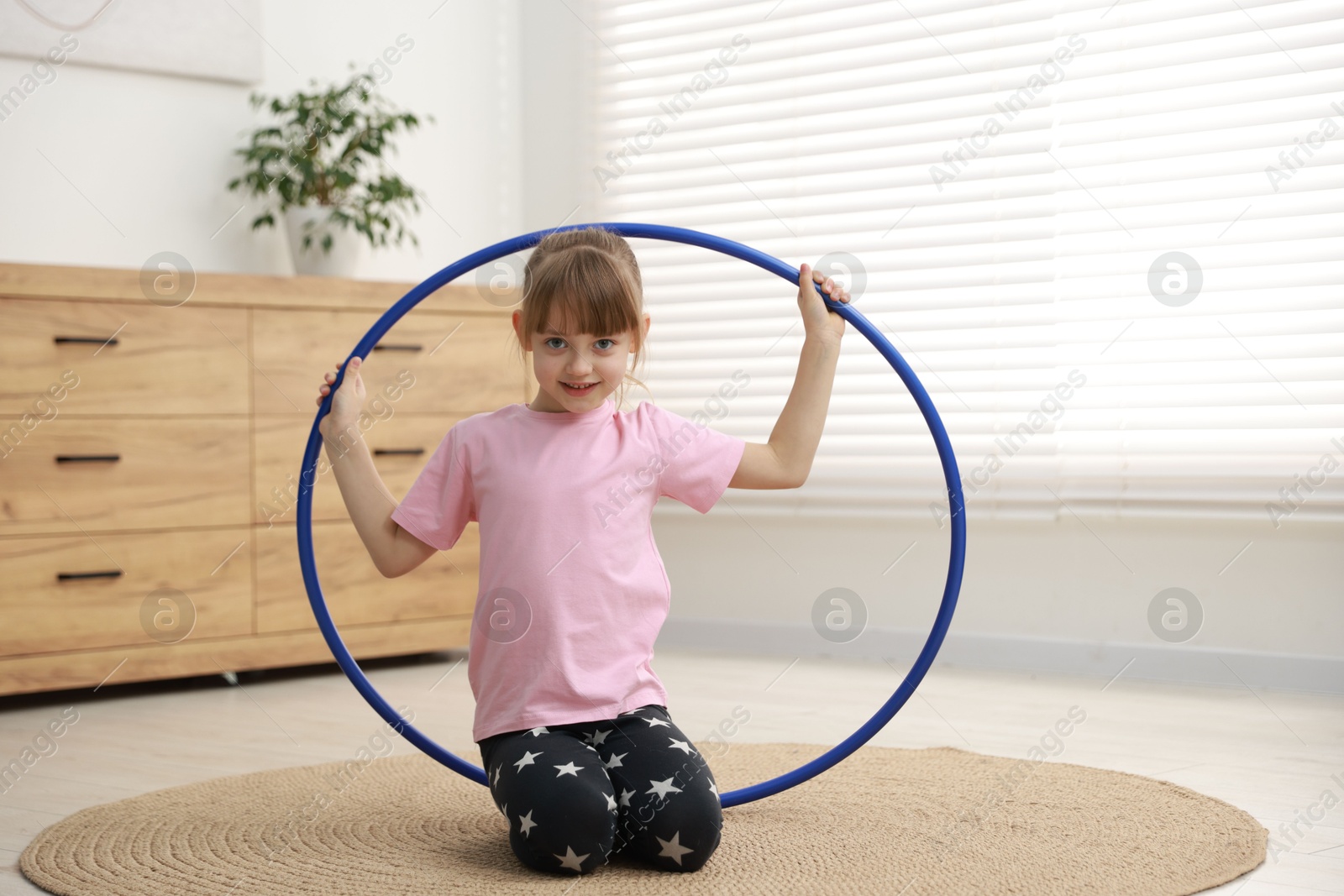 Photo of Cute little girl with hula hoop on floor at home