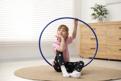 Photo of Cute little girl with hula hoop on floor at home