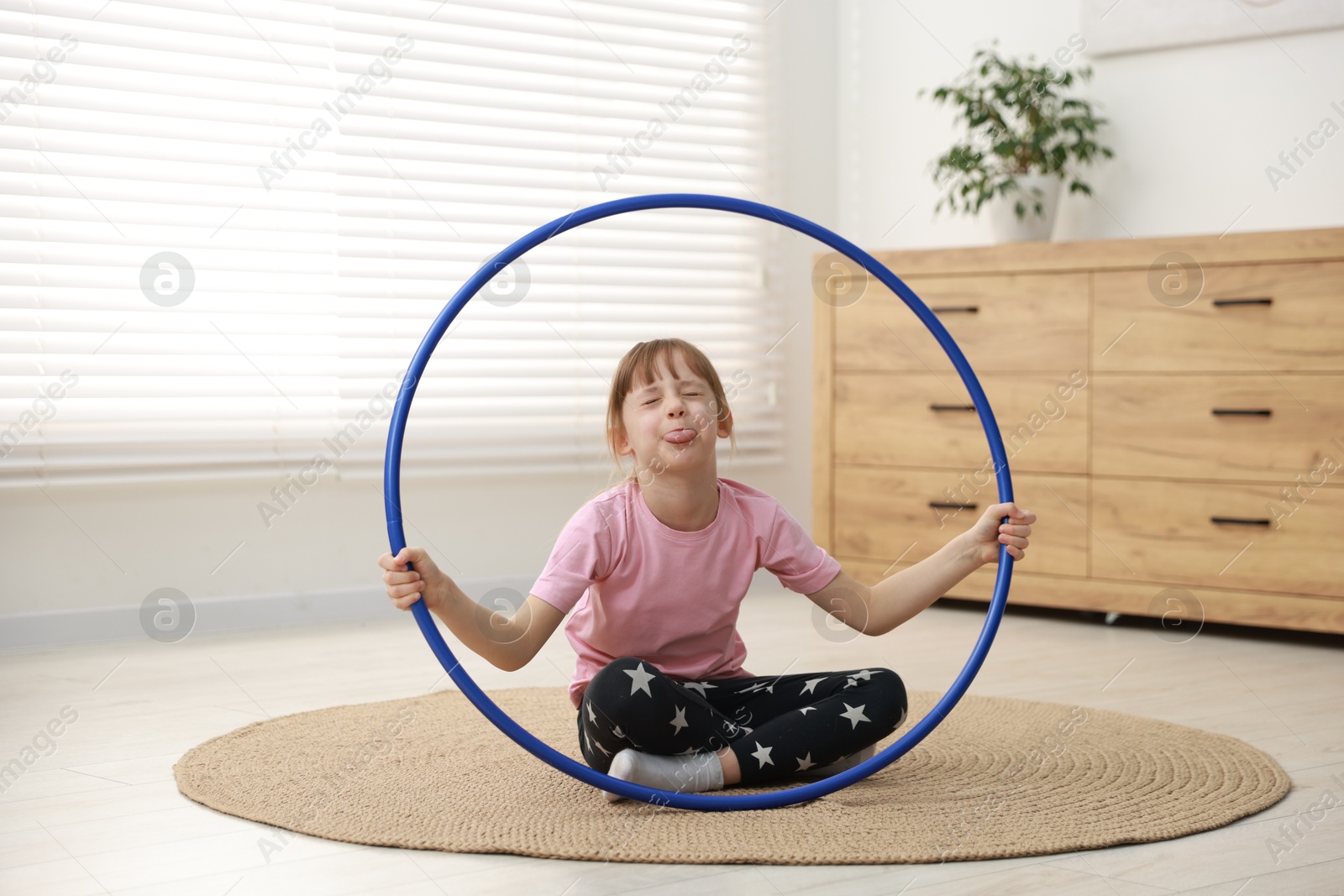 Photo of Cute little girl with hula hoop on floor at home