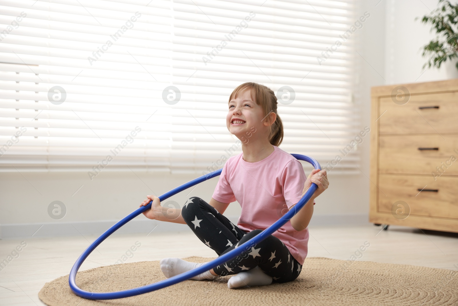 Photo of Cute little girl with hula hoop on floor at home