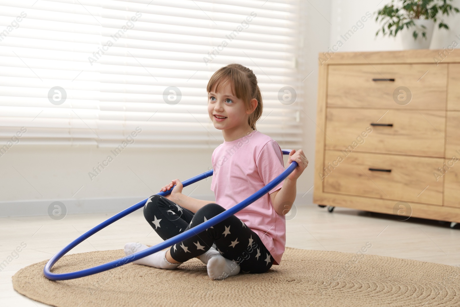 Photo of Cute little girl with hula hoop on floor at home