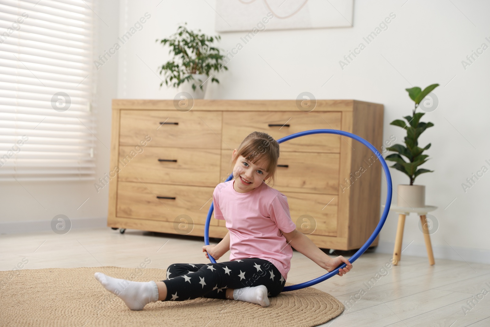 Photo of Cute little girl with hula hoop on floor at home