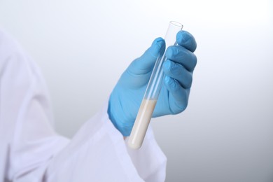 Photo of Laboratory testing. Scientist holding test tube with liquid against light background, closeup