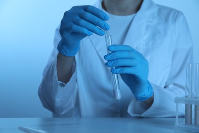 Photo of Laboratory testing. Scientist dripping liquid into test tube at table, closeup. Toned in blue