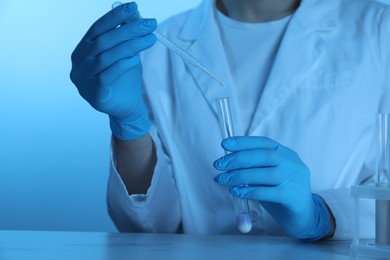 Photo of Laboratory testing. Scientist dripping liquid into test tube at table, closeup. Toned in blue