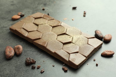 Photo of Tasty Dubai chocolate with pistachio, knafeh and cocoa beans on grey textured table, closeup