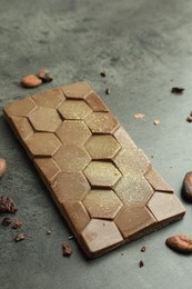 Photo of Tasty Dubai chocolate with pistachio, knafeh and cocoa beans on grey textured table, closeup