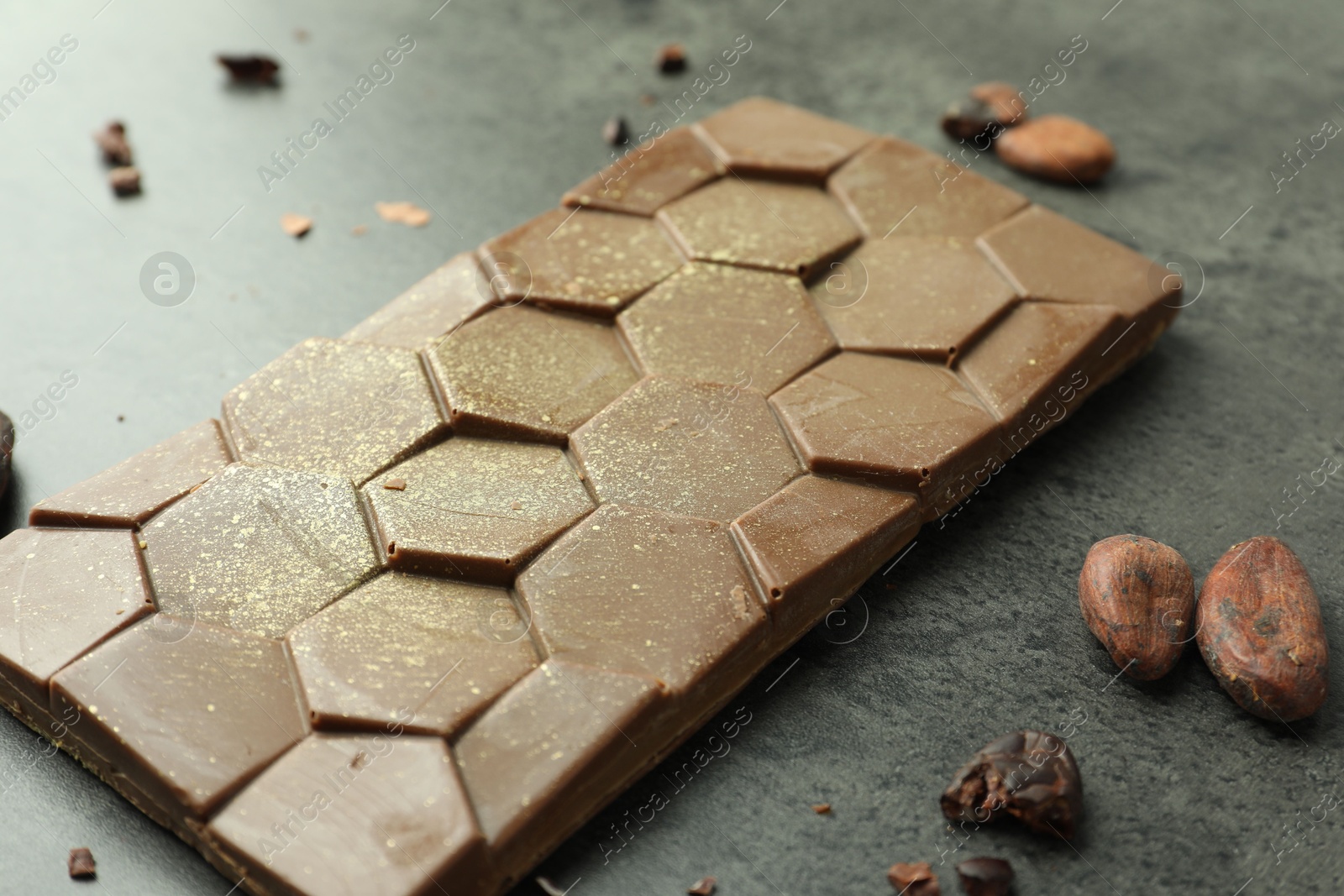 Photo of Tasty Dubai chocolate with pistachio, knafeh and cocoa beans on grey textured table, closeup